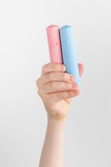 child hand holding pieces of pink and blue chalk. white and gray background with copy space