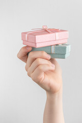 Child hand holding two gift boxes with pink and green bow. white and gray background with copy space