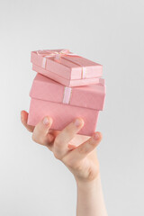 Child hand holding two gift boxes with pink bow. white and gray background with copy space