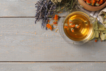 Freshly brewed tea and dried herbs on grey wooden table, flat lay. Space for text