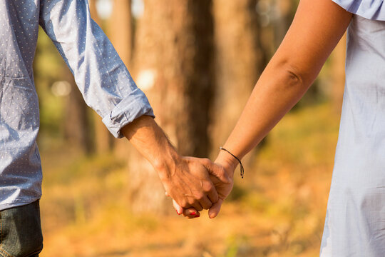 couple holding hands and walking in the forest
