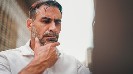 Mature businessman with neat beard wearing white shirt user on laptop pc computer sit at cafe outdoors. Successful man sitting at cafe table outdoors on nature Mobile office freelance