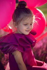 beautiful girl child of 5 years old is sitting on a pink stepladder in a pink dress in a field with pink flowers in summer at sunset.