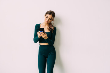 Attractive young woman with a fitness mat using mobile phone at the yoga studio