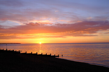 View of a beautifully colourful seaside sunset across a beach silhouette.