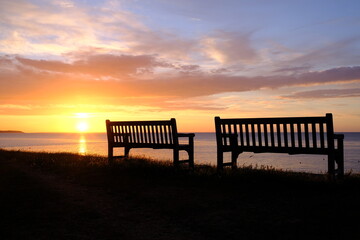 Fototapeta na wymiar Silhouette of two benches set against a beautiful seaside sunset.