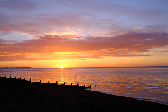 View of a beautifully colourful seaside sunset across a beach silhouette.