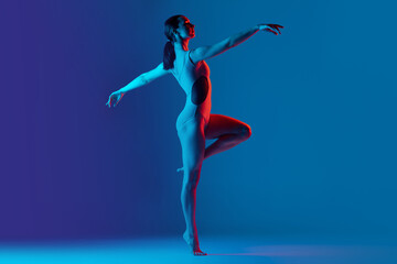 Portrait of young sportive girl doing stretching exercises isolated over blue studio background in neon light. Dancing moves