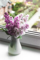 Still life on the windowsill blooming lilac in a white vase. Spring flowers, retro style