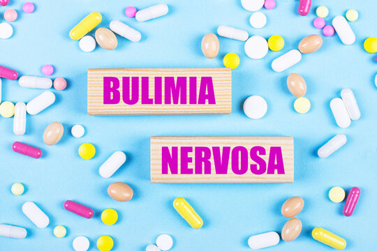 On a light blue background, multi-colored pills and wooden blocks with the text BULIMIA NERVOSA. Pharmaceutics. Medical concept.