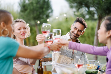 Handsome hispanic man toasting glass of wine with friends, during summer dinner in the garden