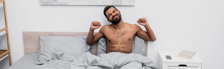 shirtless african american man with dyed hair stretching in bed, banner.