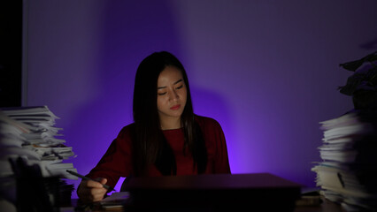 Stressed young asian woman sitting work overtime doing late time business at office in night on desk, Exhausted businesswoman concept.