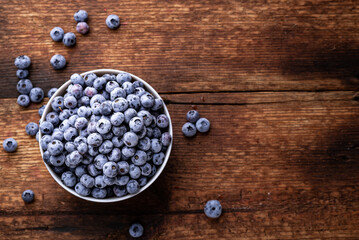 Fresh blueberries in a bowl on a brown wooden background. Place for your text.