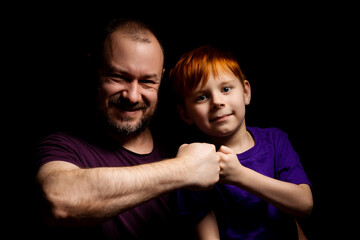 Dad and son are smiling and banging their fists against each other on a black background. Parent-child interaction. Father's day concept.