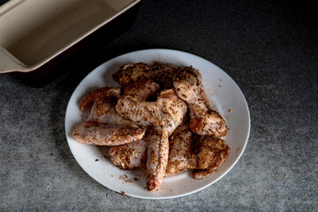 Raw chicken wings with spices on a white plate on the kitchen table. Preparing for barbecuing.