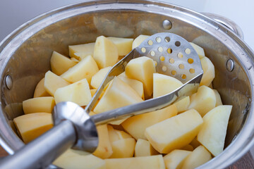 Potato masher in a pot with raw chopped potatoes