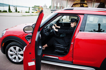 Portrait of beautiful blonde sexy fashion woman model in cap and in all black with bright makeup sit and drive red city car.
