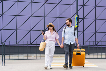 Couple of tourists travelers with tickets and an orange plastic orange suitcase cross a pedestrian crossing heading for a boarding. travel summer vacation voyage 