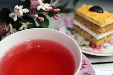 A cup of tea large smooth and a cake on a wooden table with flowers in the background
