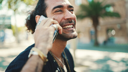 Attractive italian guy with ponytail and stubble is using mobile phone sitting on bench at old...