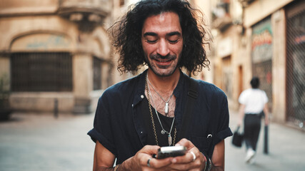 Young attractive italian guy with long curly hair and stubble is using mobile phone at old...