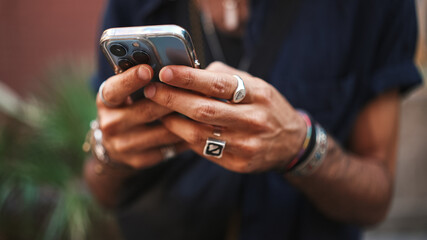 Close-up of male hands in bracelets and rings. Man is using mobile phone. Guy writes message on his smartphone