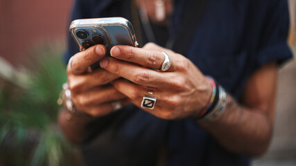 Close-up of male hands in bracelets and rings. Man is using mobile phone. Guy writes message on his...