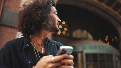 Italian guy with long curly hair and stubble is using mobile phone at old buildings background....