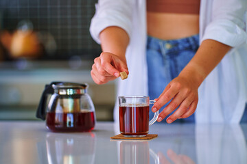 Female adding cane brown sugar cube to black tea at home kitchen