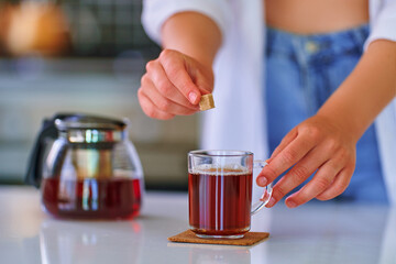 Female adding cane brown sugar cube to black tea at home kitchen