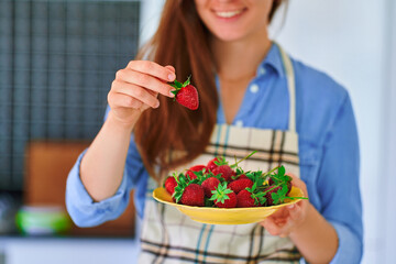 Female holding plate with fresh ripe organic strawberries at home kitchen