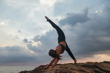 Young woman does asana yoga for healthy lifestyle on tropical coast beach at sunset.