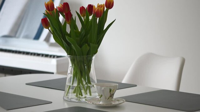 Beautiful tulips in vase on table and coffee cup in modern living room in morning
