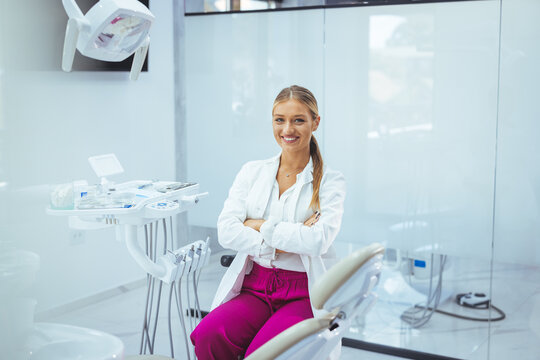 Portrait Of Beautiful Professional Female Stomatologist Posing In Clinic Interior, Happy Dentist Lady Standing With Folded Arms And Smiling At Camera, Ready For Check Up