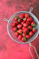 Juicy strawberry in a strainer. Red textured background with copy space. Simple composition still life with summer berries. Eating healthy concept. 