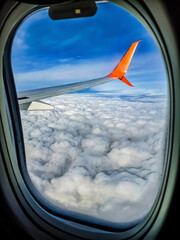 View of white fluffy clouds and airplane wing through plane window, close-up. Cloudscape behind the...