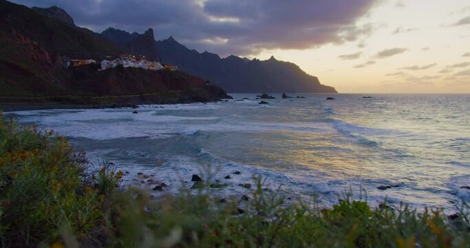 Sunset over Atlantic Ocean, north Tenerife, Almaciga black sandy beach and village. Vegetation in the foreground.