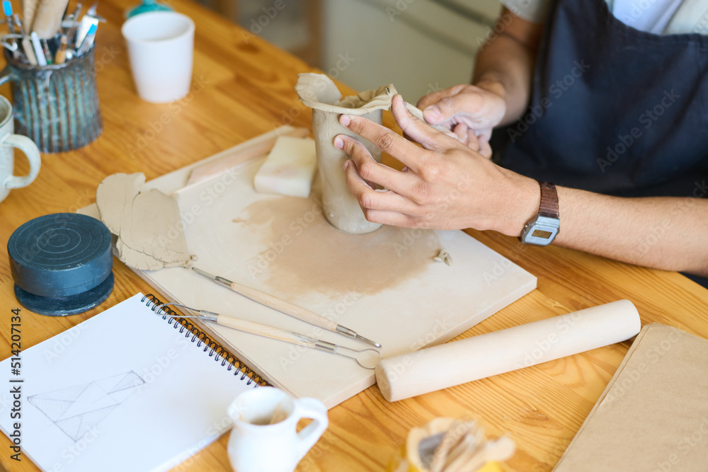 Aufkleber hands of young male potter forming shape of vase or jug while sitting by table and working over new 