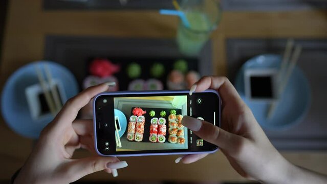 Girl take pictures of sushi in cosy japanese restaurant, using smartphone. Female hands take photos of food by modern smartphone. Close up, 4K