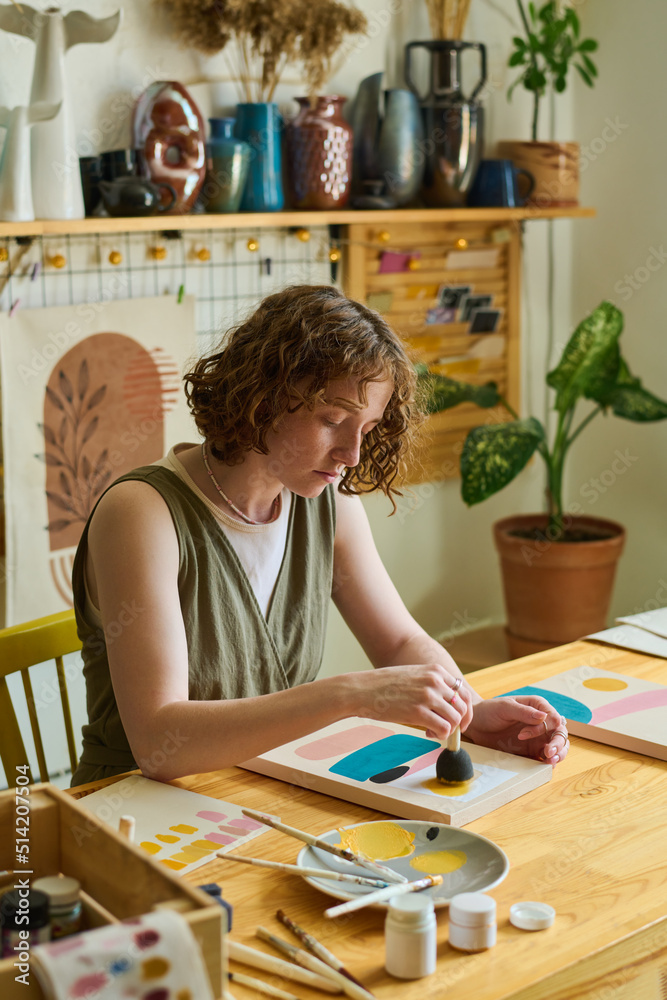 Poster creative female artist in casualwear using sponge for applying color on paper while working over new