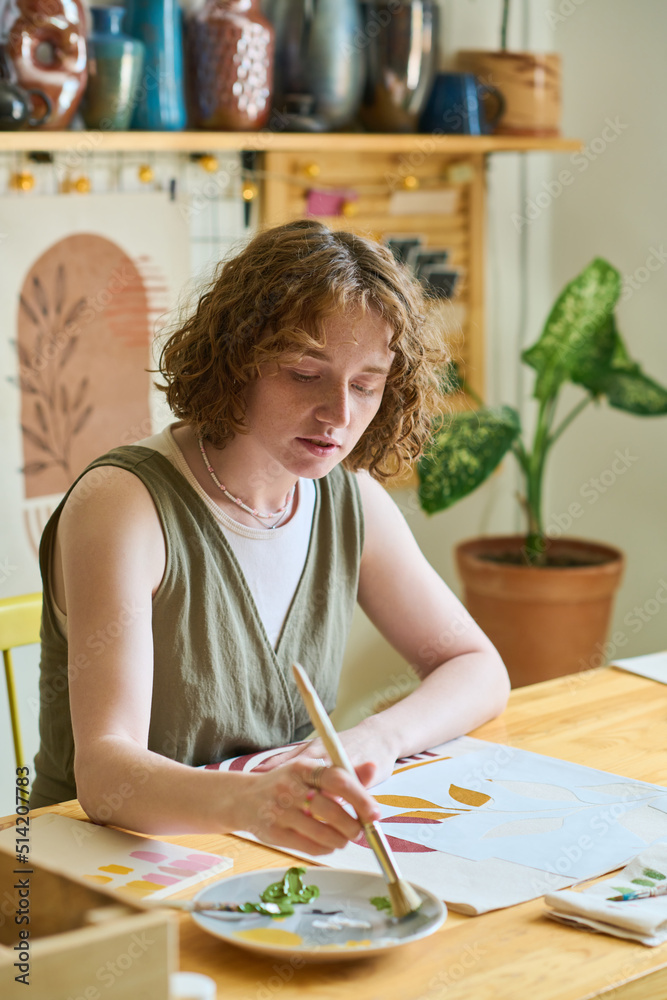 Aufkleber young female putting paintbrush in plate with mixed gouache of various colors while creating new abs