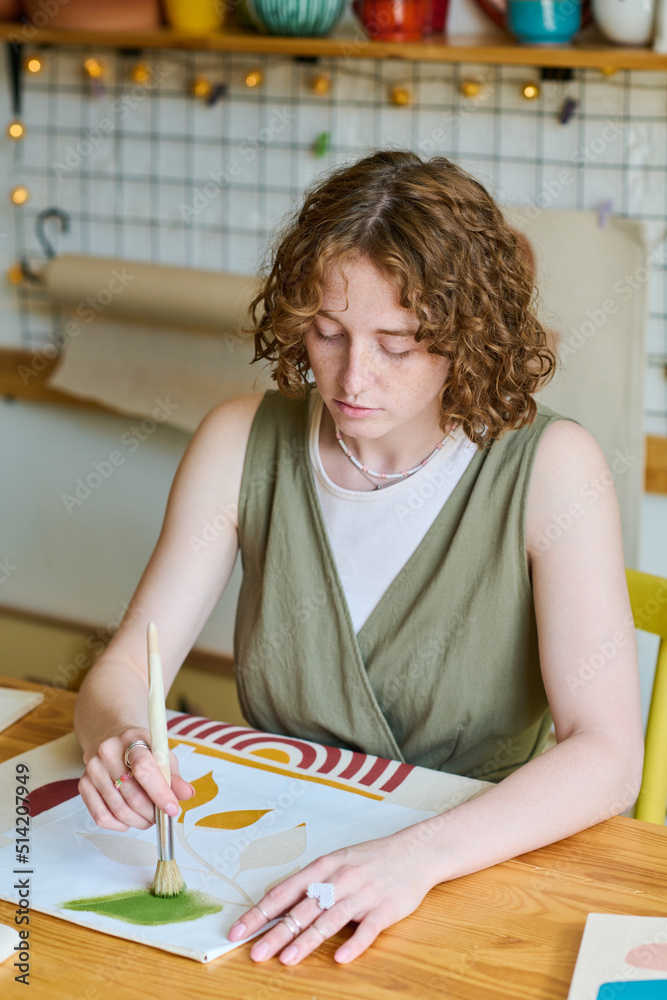 Poster diligent and creative girl in casualwear holding paintbrush over paper during process of creating ne