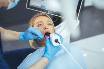 European young woman sitting in medical chair while dentist fixing her teeth at dental clinic....