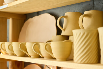 Part of display consisting of several wooden shelves with handmade earthenware such as cups, mugs and plates in souvenir shop