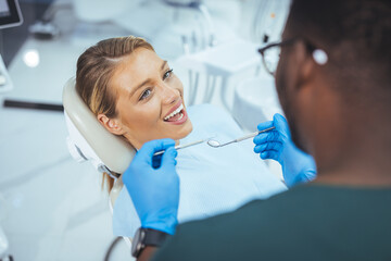 Dentist and patient in dentist office. Over the shoulder view of a dentist examining a patients teeth in dental clinic. Female having her teeth examined by a dentist.