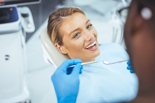 European young woman sitting in medical chair while dentist fixing her teeth at dental clinic. Image of satisfied young woman sitting in dental chair at medical center