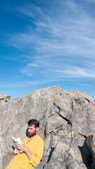 Hombre blanco barbudo leyendo un libro entre rocas en playa rocosa