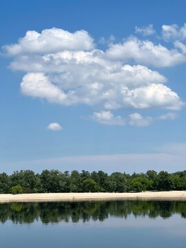 Lake calm water and sand beach at sunny summer day. Blue sky and clouds over the river.