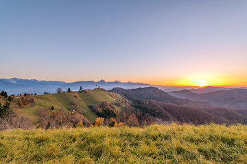Obraz premium Church on the hill at sunrise. Beautiful scenery at Jamnik, Slovenia. Panoramic view of the mountains behind the church in the early morning.